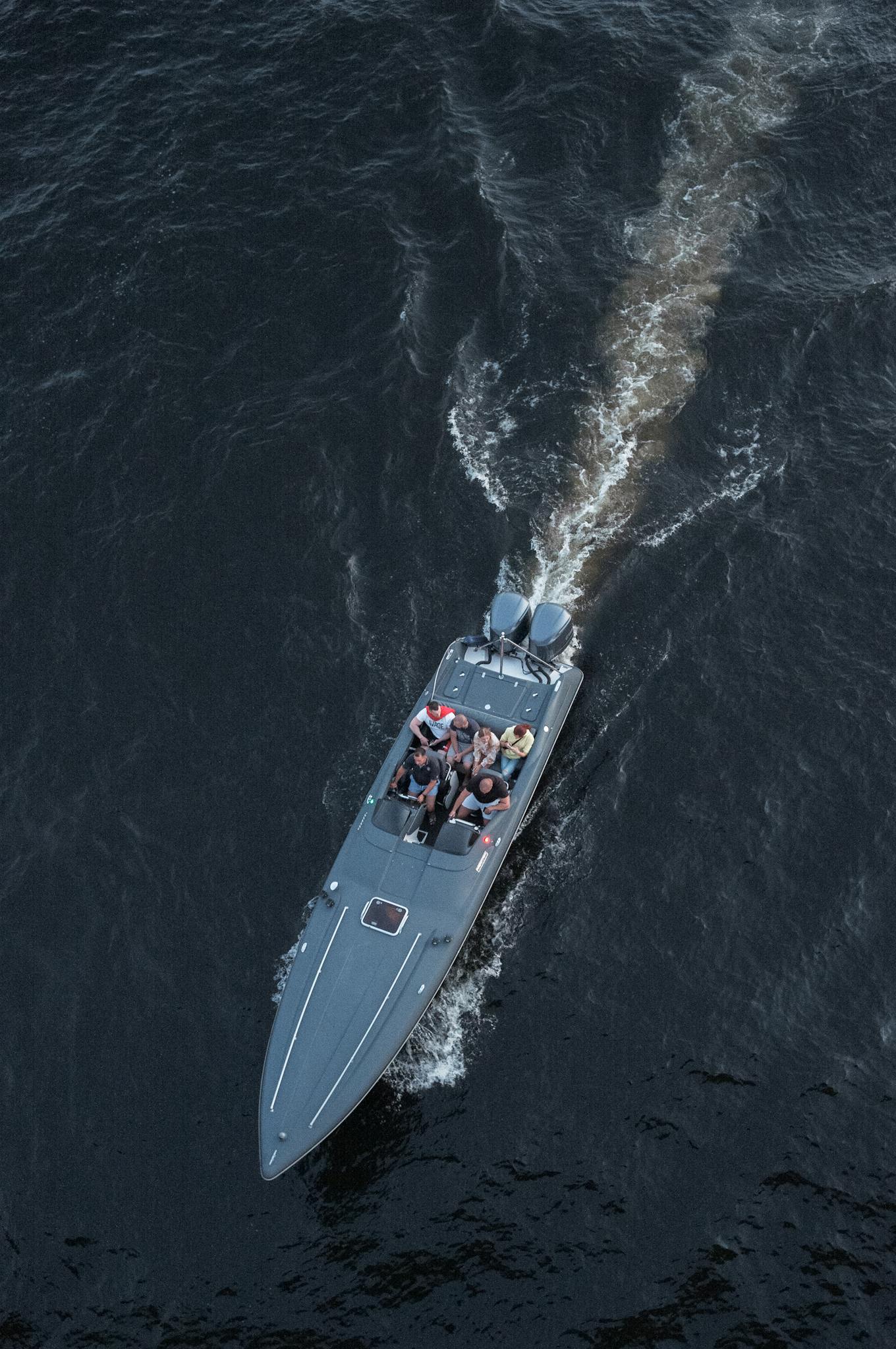 Aerial view of a speedboat cutting through dark waters with passengers on board.